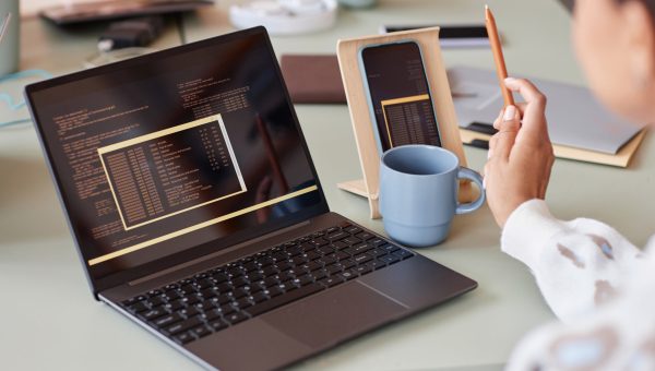 Close up of unrecognizable young woman using laptop with programming code at workplace in office, copy space